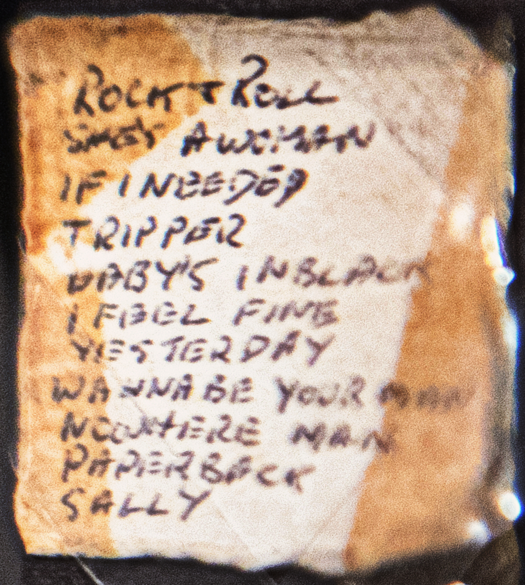 Handwritten Beatles song list with shorthand titles including Yesterday, Nowhere Man and Paperback, photographed at an LBJ Library exhibition